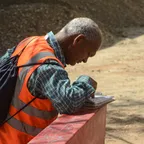 A worker in an orange high-visibility vest writing on a sheet of paper at an outdoor site