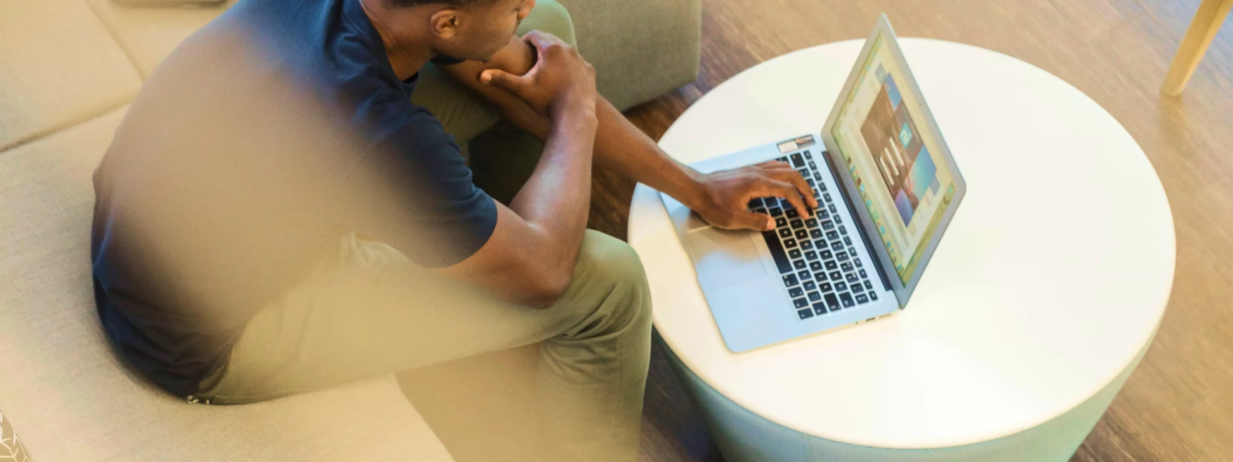 Person sitting on a couch using a laptop on a round white table.