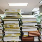 Tall stacks of paper files and folders piled up in an office